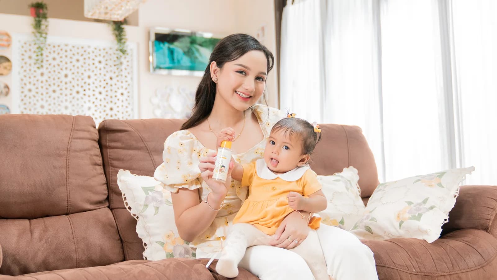 Mama memakaikan Baby Hair Vitamin Lotion pada rambut si Kecil di sofa