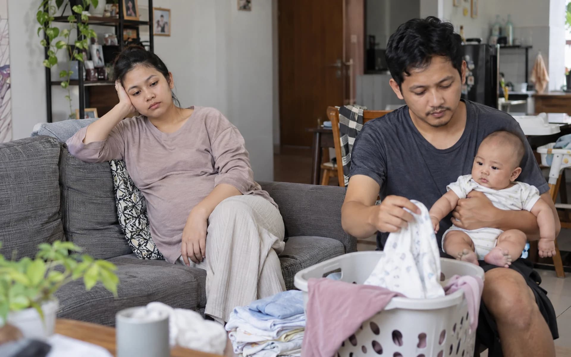 Ibu dan ayah duduk bersama bayi mereka di ruang tamu